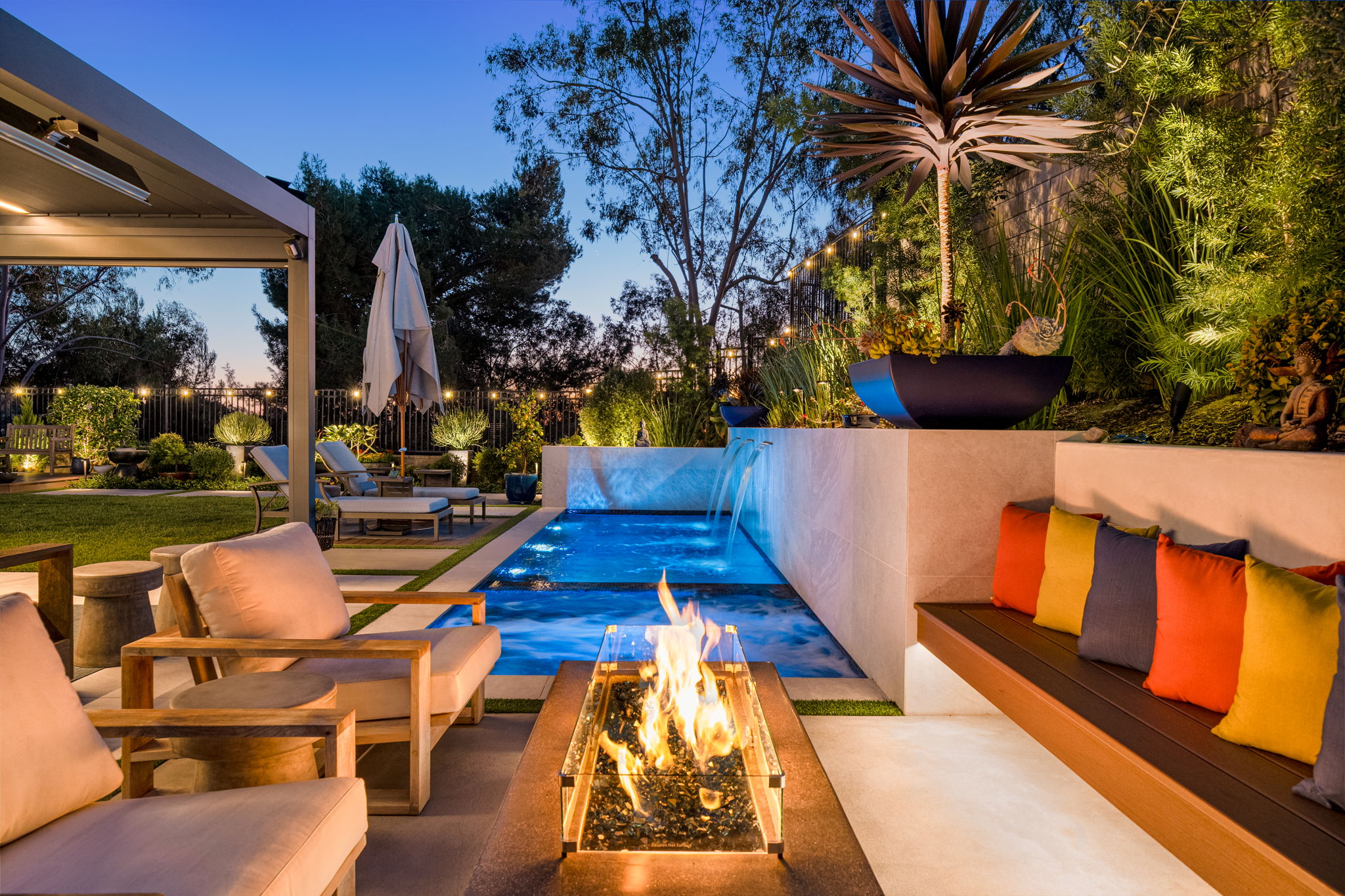 Poolside lounge seating with colorful pillows and a fire table at dusk